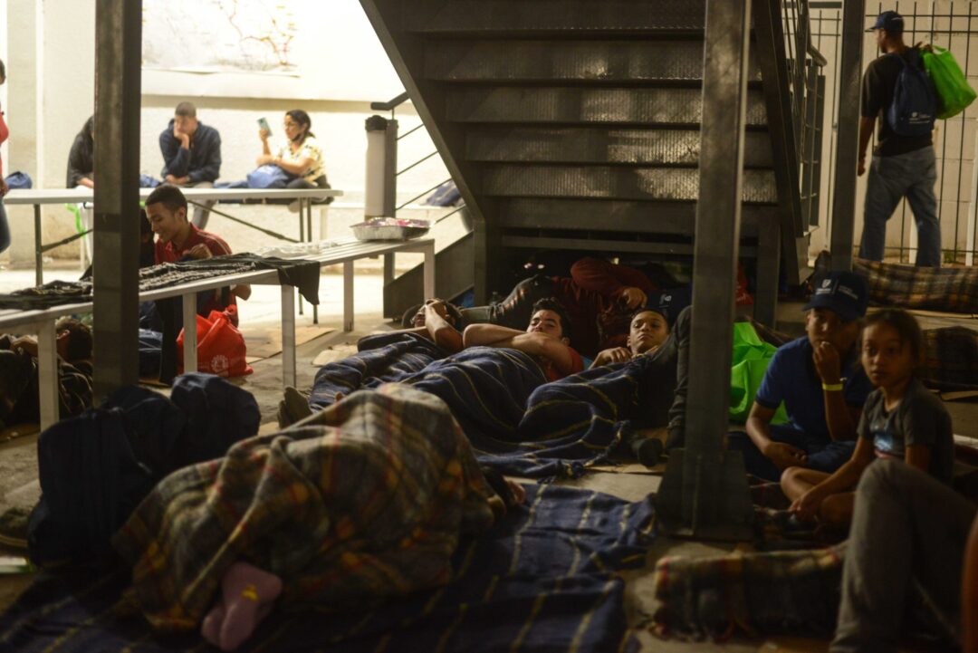 Familias venezolanas durmiendo sobre el piso en un refugio improvisado, cubiertas con cobijas